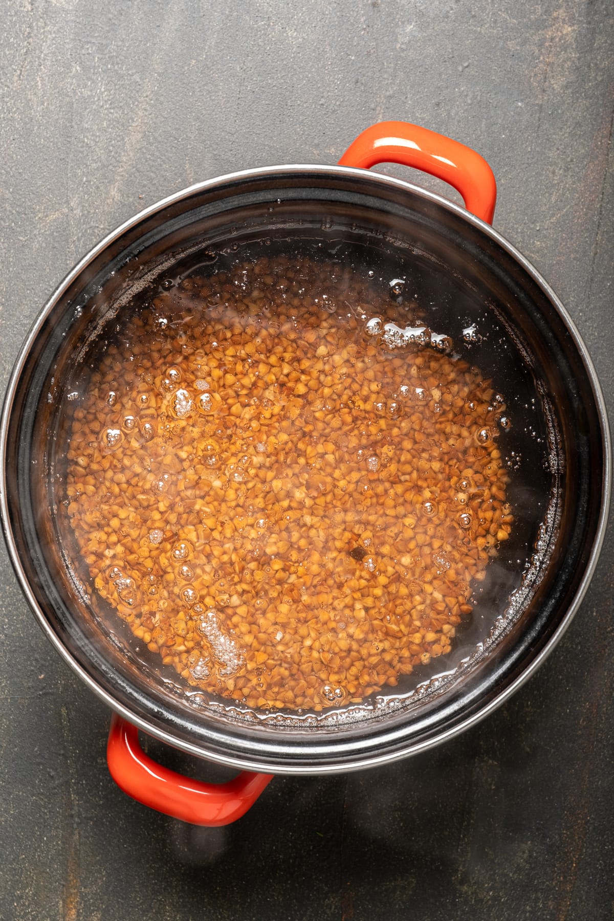 荞麦涂料和水在黑平底锅用红色手柄。
