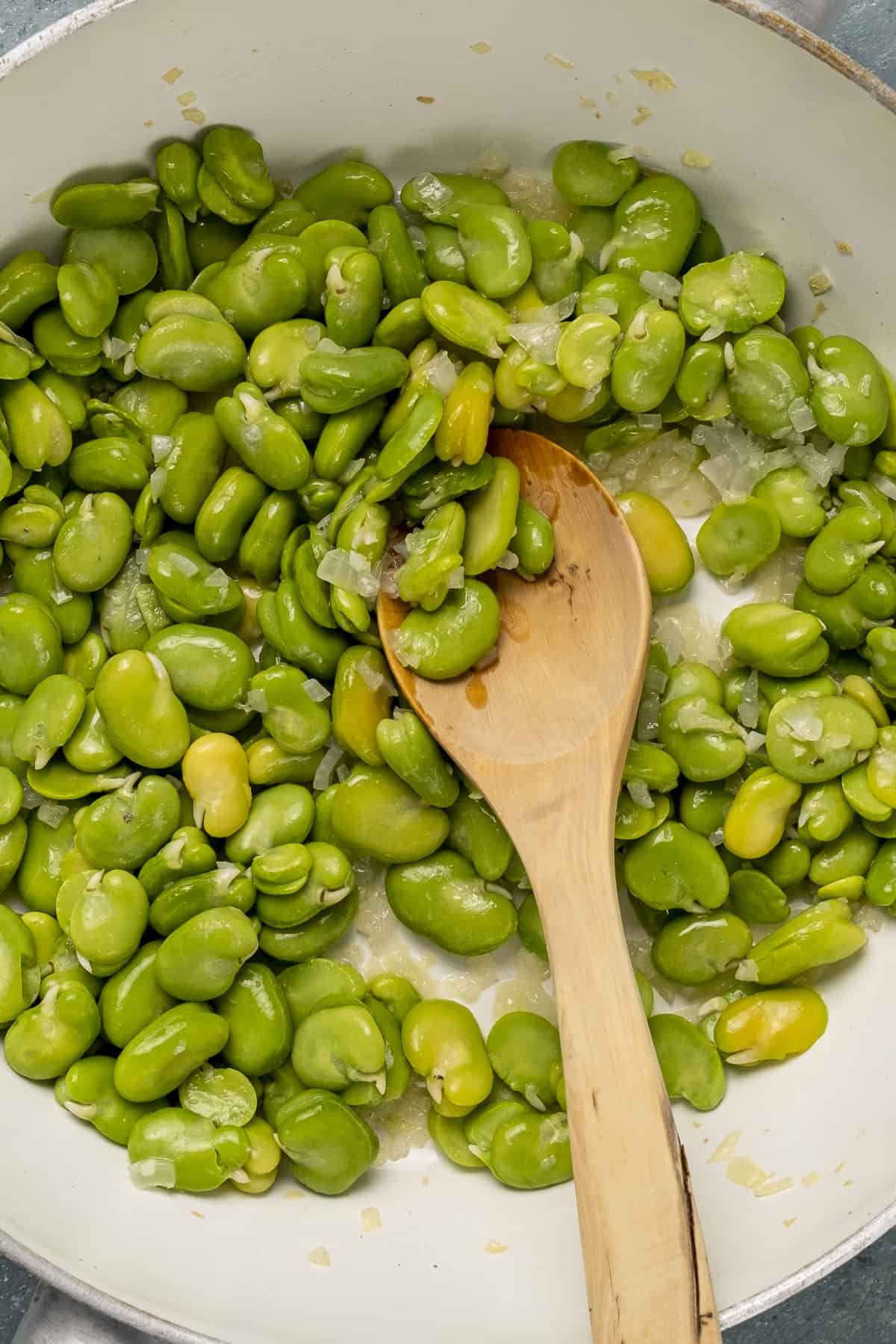 绿色的新鲜蚕豆在平底锅里煮，木勺在里面。
