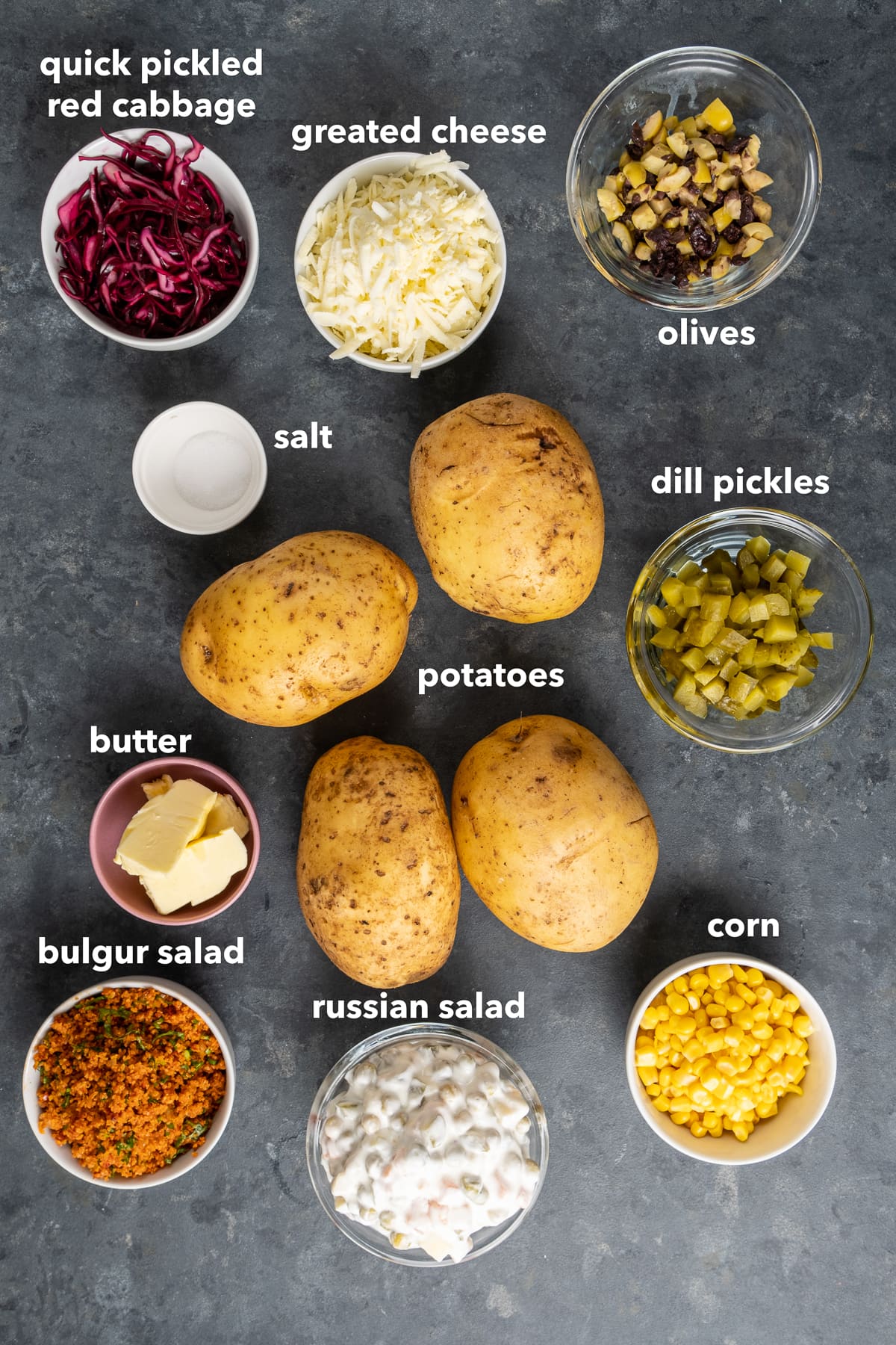 土豆，莳萝泡菜，红卷心菜，磨碎的奶酪，盐，切碎的橄榄，俄罗斯沙拉，磨碎的沙拉和黑色背景的黄油。