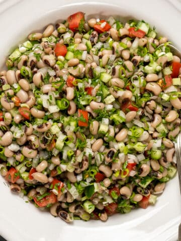 黑眼豌豆沙拉，蔬菜和香草放在一个白色的碗里，里面有勺子。
