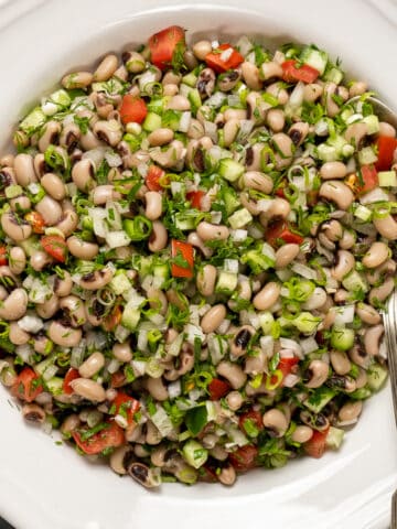 Black eyed pea salad with vegetables and herbs in a white bowl and a spoon in it.