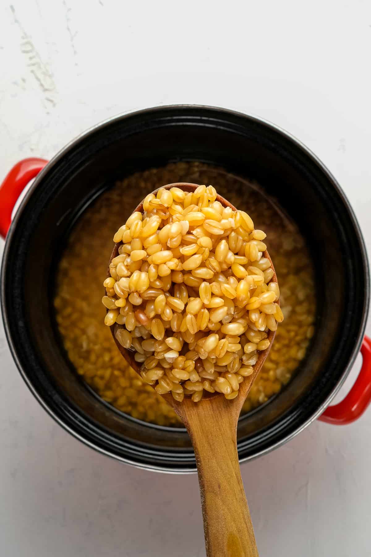 用木勺煮熟的小麦浆果，平底锅上有黑色的红把手珐琅。