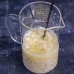 杏仁奶和醋的混合物在一个玻璃量杯和搅拌勺里面。