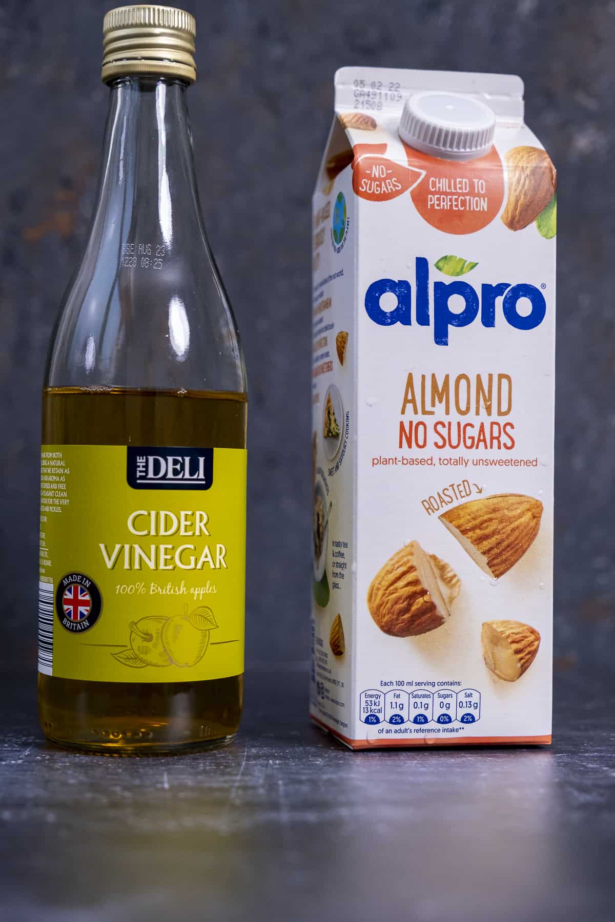 一盒Alpro杏仁奶和一瓶苹果醋，背景是深色的。