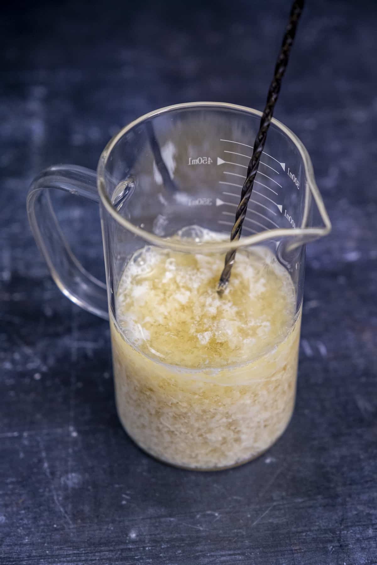 杏仁奶和醋的混合物在一个玻璃量杯和搅拌勺里面。