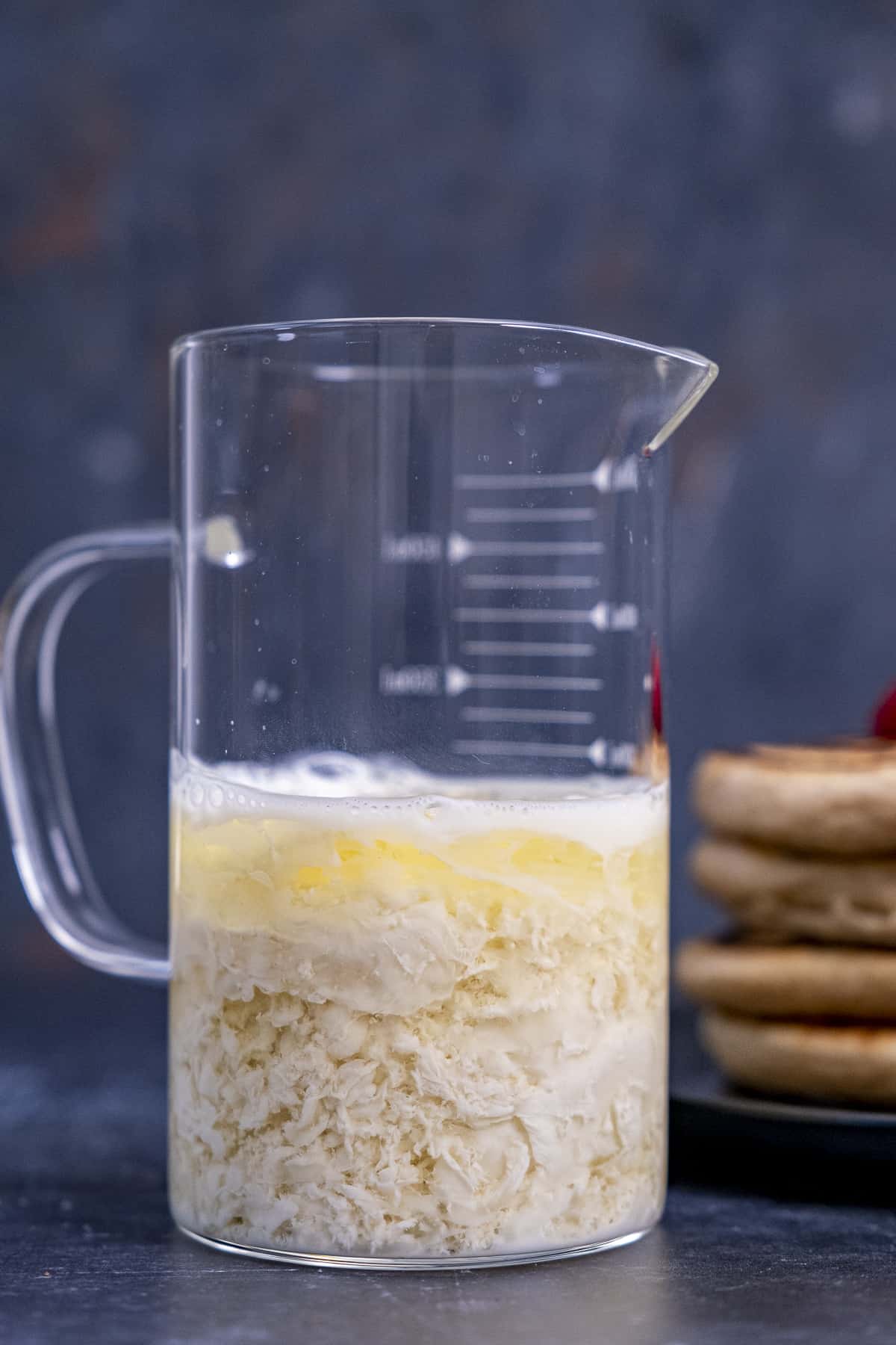 不含乳制品的脱脂牛奶放在一个玻璃量杯里，煎饼放在后面的黑色背景上。