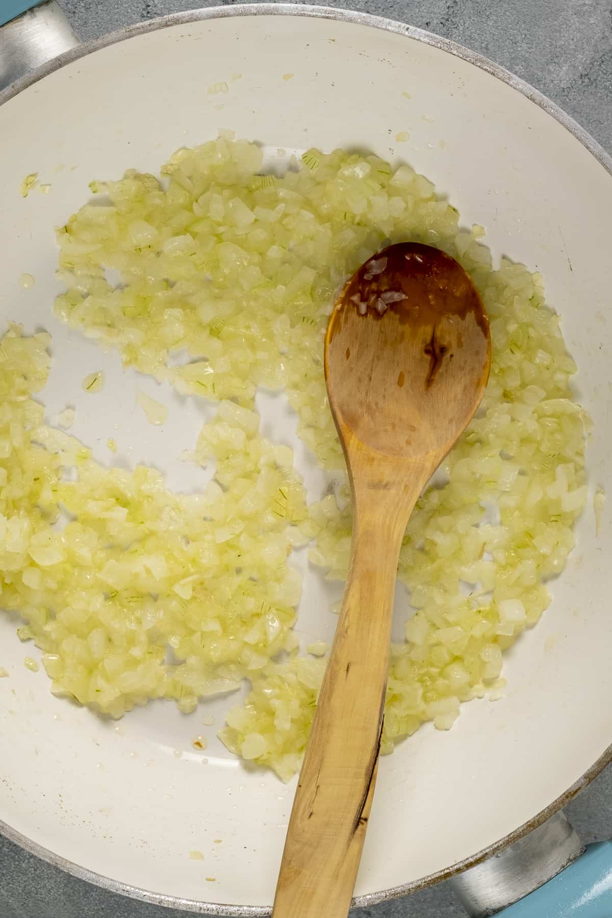 将切碎的洋葱放入白色平底锅中，将木勺放入锅中。