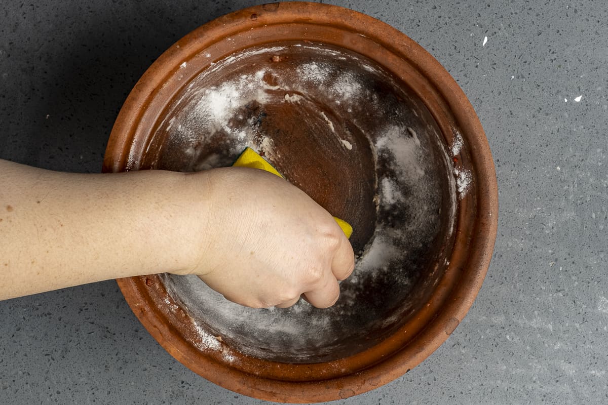 一只手用小苏打和海绵清洗陶罐。