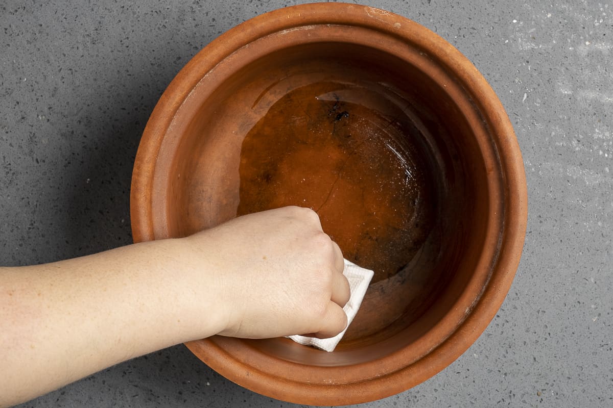 用纸巾和油给陶罐上油的手。