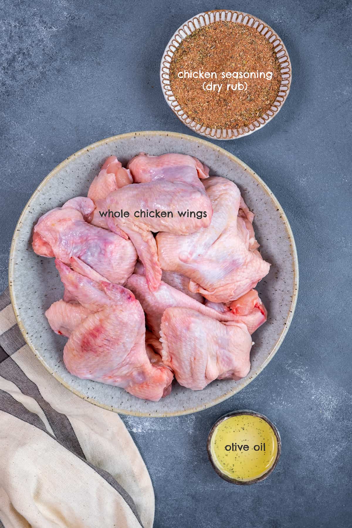一整只生鸡翅放在碗里，鸡肉调味料和橄榄油放在小碗里。