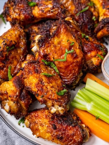 Golden brown chicken wings on a plate with carrots, celery sticks and a dip sauce.