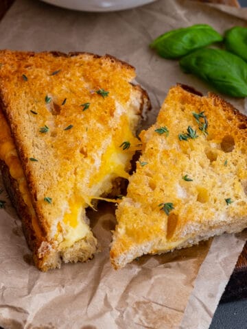 Grilled cheese sandwiches garnished with thyme and basil leaves behind them.