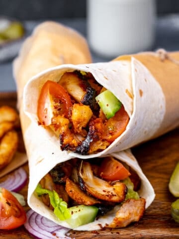 Chicken doner wraps on a wooden board, pickled, French fries, tomato and onion slices on the side.